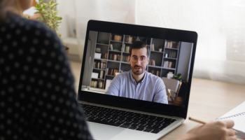 Close up back view of woman looking at a laptop screen talking on a video call with a man 